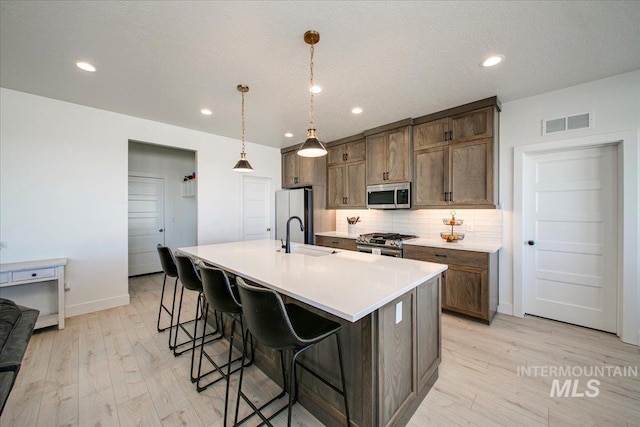 kitchen with stainless steel appliances, light wood-style flooring, visible vents, and tasteful backsplash