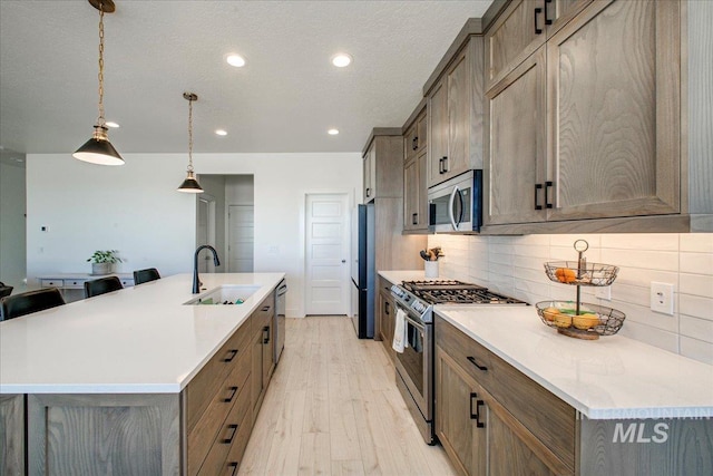 kitchen featuring light wood-style flooring, a sink, recessed lighting, decorative backsplash, and appliances with stainless steel finishes