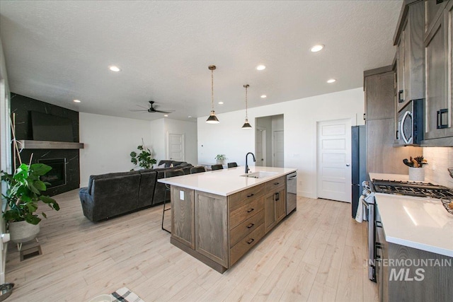 kitchen with stainless steel appliances, a sink, light wood-style floors, ceiling fan, and an island with sink