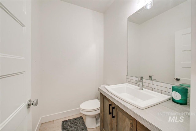 half bath with toilet, baseboards, backsplash, wood finished floors, and vanity
