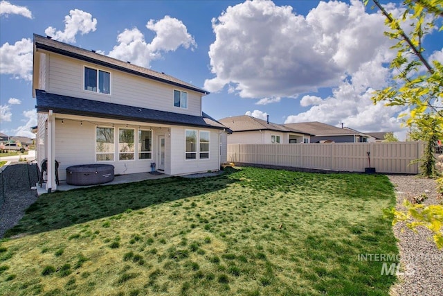 rear view of house with a fenced backyard, a yard, a hot tub, and a patio
