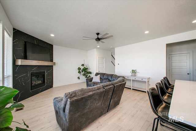 living room featuring light wood-style flooring, a textured ceiling, recessed lighting, ceiling fan, and a high end fireplace