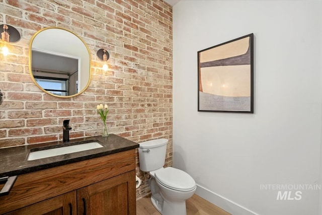 12975 Shasta Daisy Way, Nampa, ID 83686 - bathroom with vanity, baseboards, wood finished floors, toilet, and brick wall