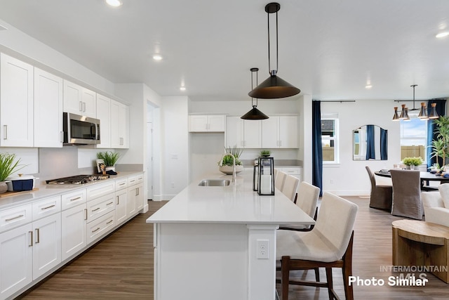 kitchen featuring white cabinets, dark hardwood / wood-style floors, an island with sink, decorative light fixtures, and stainless steel appliances