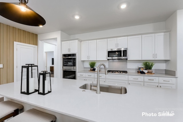 kitchen featuring white cabinetry, sink, wood walls, a kitchen bar, and appliances with stainless steel finishes