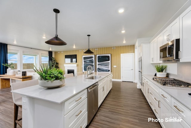 kitchen with white cabinets, hanging light fixtures, sink, an island with sink, and appliances with stainless steel finishes