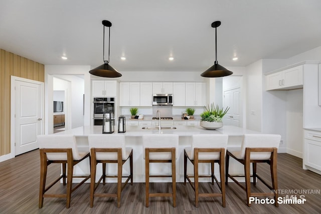 kitchen with a center island with sink, white cabinets, decorative light fixtures, and appliances with stainless steel finishes