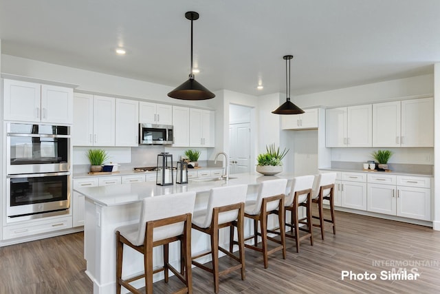 kitchen with a kitchen bar, stainless steel appliances, dark wood-type flooring, a center island with sink, and white cabinets