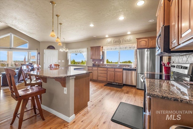 10395 Willis Rd, Middleton, ID 83644 - kitchen featuring a breakfast bar, stainless steel appliances, brown cabinetry, a textured ceiling, and a kitchen island