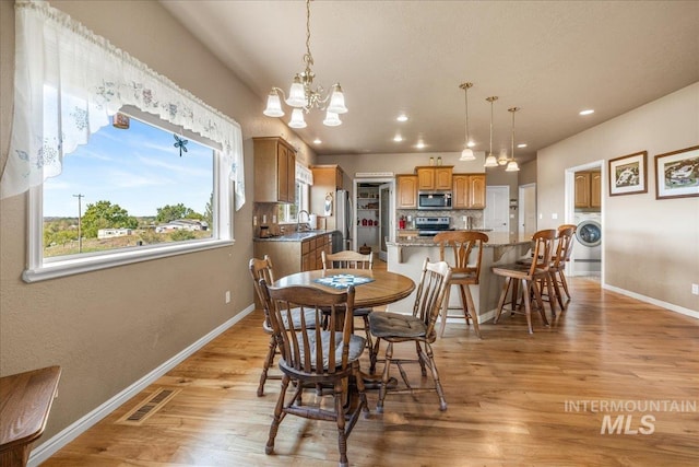 10395 Willis Rd, Middleton, ID 83644 - dining area featuring visible vents, baseboards, light wood-style floors, a chandelier, and washer / clothes dryer