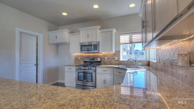 kitchen with light stone counters, tasteful backsplash, appliances with stainless steel finishes, white cabinetry, and a sink