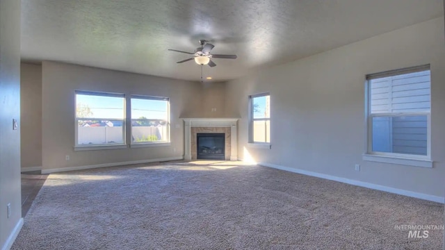 unfurnished living room featuring carpet floors, a ceiling fan, a textured ceiling, a tile fireplace, and baseboards