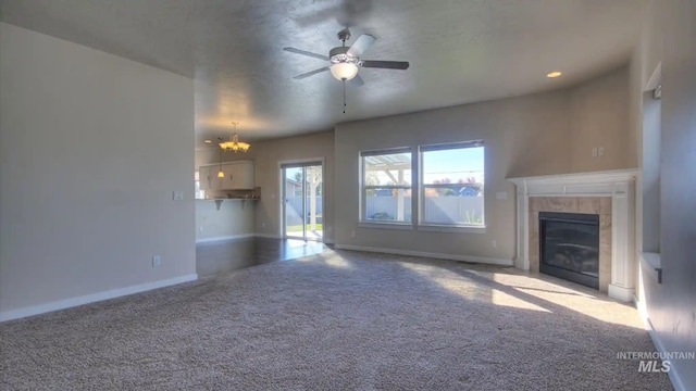 unfurnished living room with carpet, a fireplace, baseboards, and ceiling fan with notable chandelier