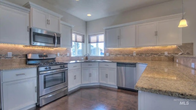 kitchen with white cabinets, light stone counters, appliances with stainless steel finishes, a sink, and backsplash