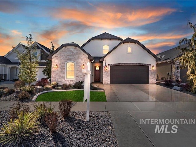 view of front of house with an attached garage, stone siding, driveway, and stucco siding