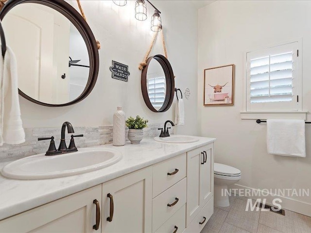 full bathroom with double vanity, toilet, a healthy amount of sunlight, and a sink