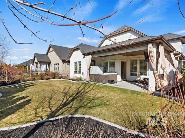 rear view of house featuring stucco siding, fence, a lawn, and a hot tub