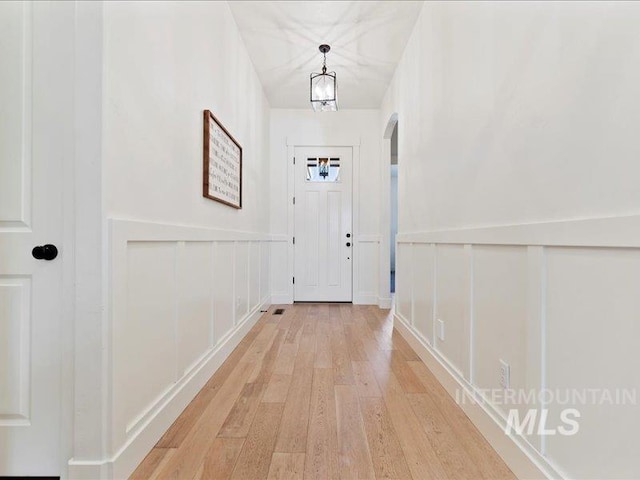 doorway featuring light wood finished floors, a decorative wall, arched walkways, and a wainscoted wall