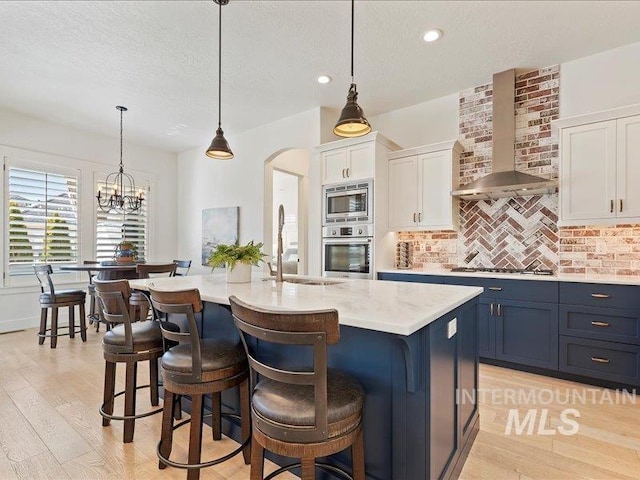 kitchen featuring wall chimney range hood, backsplash, arched walkways, appliances with stainless steel finishes, and light countertops