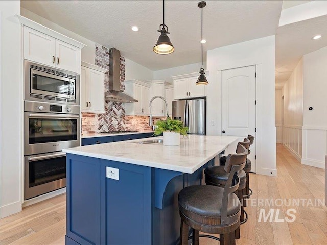 kitchen with stainless steel appliances, light wood-style flooring, decorative backsplash, and wall chimney range hood