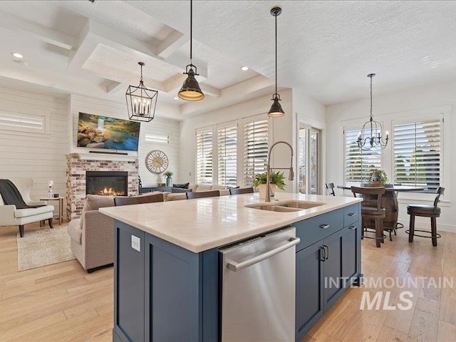 kitchen with light wood finished floors, an inviting chandelier, a fireplace, a sink, and stainless steel dishwasher