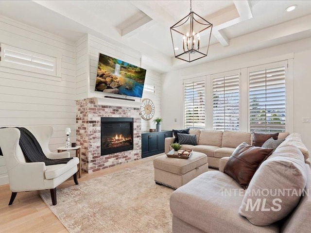 living area with beam ceiling, a notable chandelier, coffered ceiling, wood finished floors, and a brick fireplace