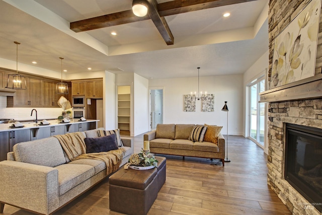 living room with sink, hardwood / wood-style floors, a fireplace, beamed ceiling, and a chandelier