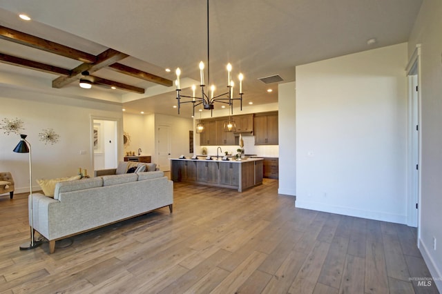 living room featuring beamed ceiling, wood-type flooring, sink, and an inviting chandelier