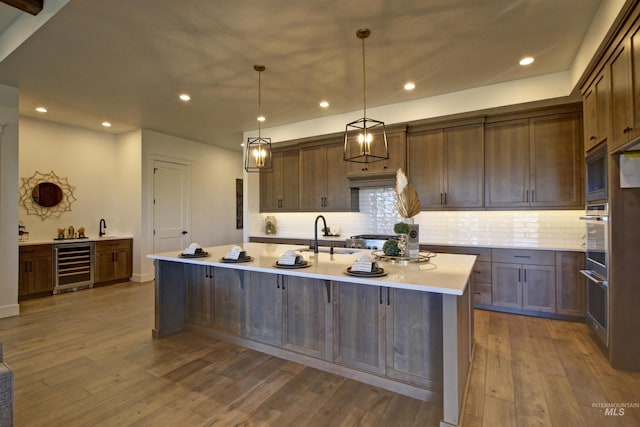 kitchen with sink, light hardwood / wood-style flooring, pendant lighting, beverage cooler, and a kitchen island with sink