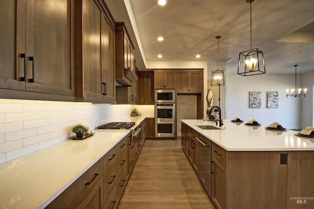 kitchen with sink, hanging light fixtures, stainless steel appliances, hardwood / wood-style floors, and decorative backsplash