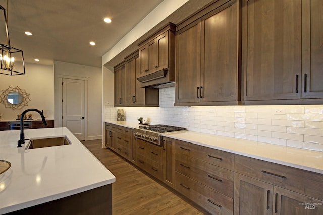 kitchen featuring decorative light fixtures, stainless steel gas stovetop, sink, backsplash, and dark hardwood / wood-style flooring