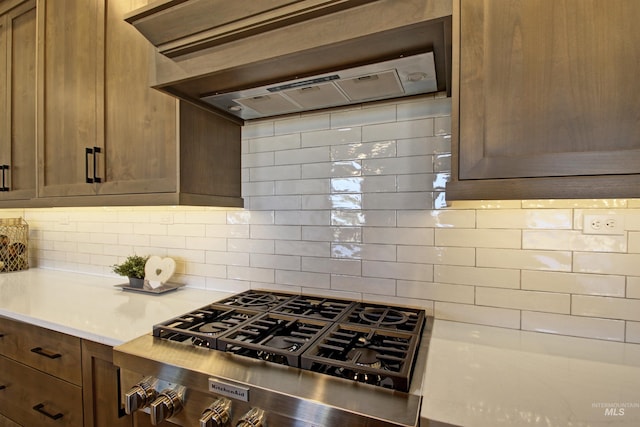 kitchen with decorative backsplash, stainless steel gas cooktop, and premium range hood