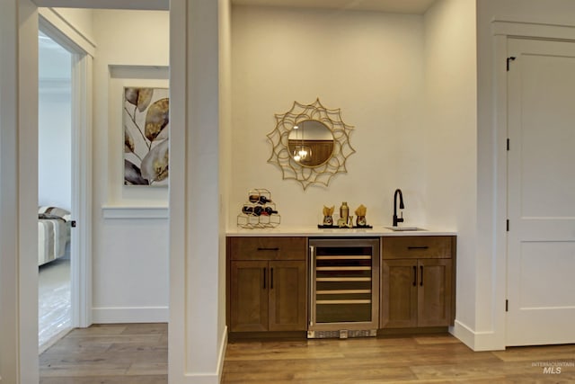 bar with sink, beverage cooler, and light wood-type flooring