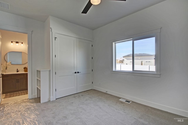 unfurnished bedroom featuring connected bathroom, sink, ceiling fan, light carpet, and a closet