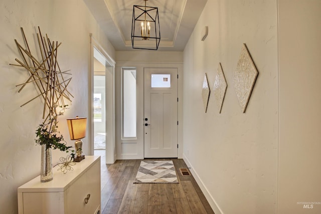 doorway to outside with a raised ceiling, wood-type flooring, a healthy amount of sunlight, and a notable chandelier