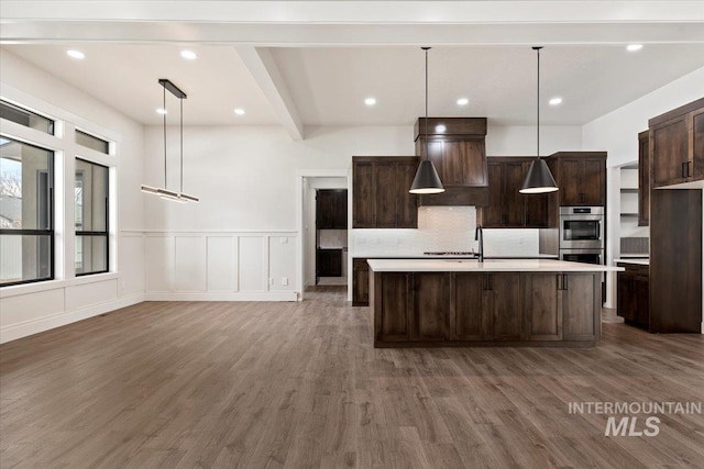 kitchen with dark brown cabinetry, wood finished floors, light countertops, double oven, and beam ceiling