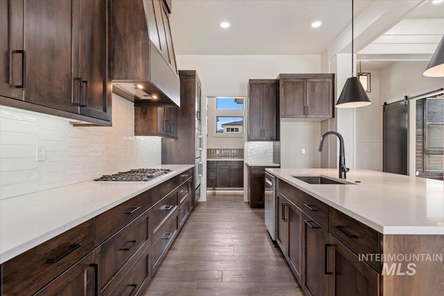 kitchen with a barn door, dark wood-type flooring, premium range hood, stainless steel gas stovetop, and a sink