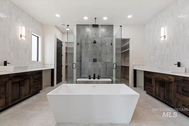 bathroom featuring a stall shower, two vanities, a sink, and tile walls