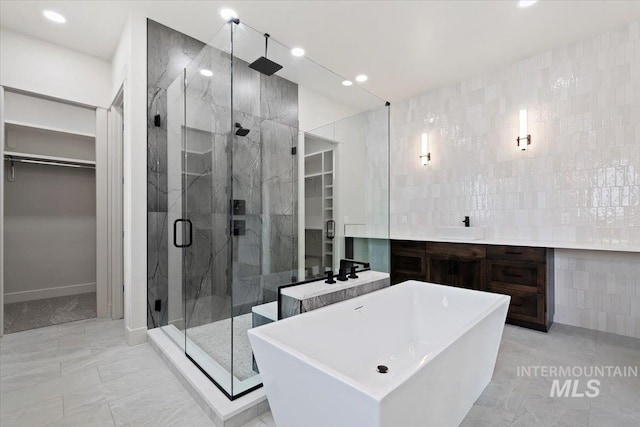 bathroom featuring marble finish floor, tile walls, a spacious closet, a stall shower, and a sink