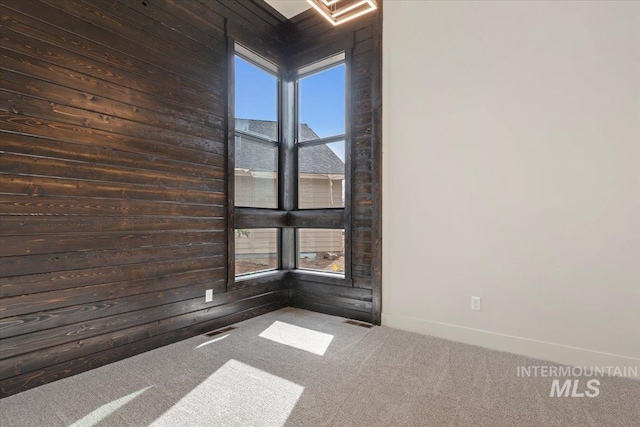 carpeted spare room featuring visible vents, wood walls, and baseboards