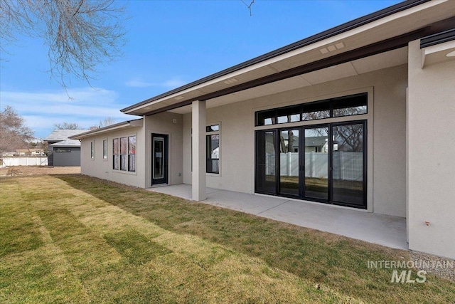 rear view of house with a lawn, a patio, and stucco siding