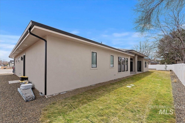 rear view of property with a lawn, fence, and stucco siding