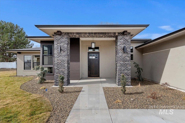 view of exterior entry featuring brick siding, a lawn, and stucco siding