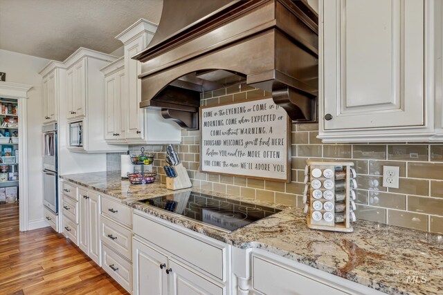 2466 Brooks Dr, Fruitland, ID 83619 - kitchen with appliances with stainless steel finishes, white cabinetry, custom exhaust hood, light stone counters, and light wood-style floors