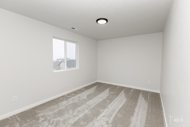 spare room featuring carpet floors, visible vents, a textured ceiling, and baseboards