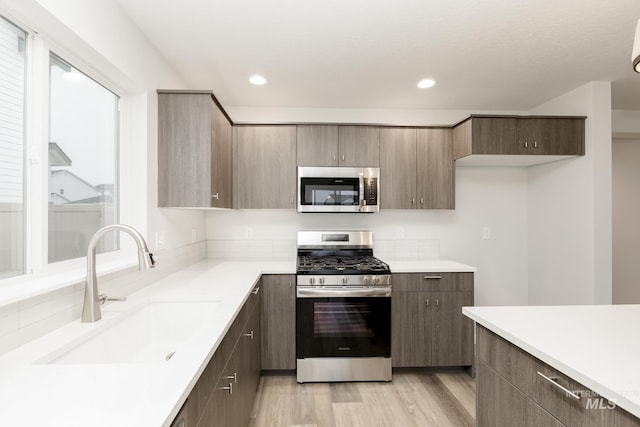 kitchen featuring light wood-type flooring, appliances with stainless steel finishes, light countertops, and a sink