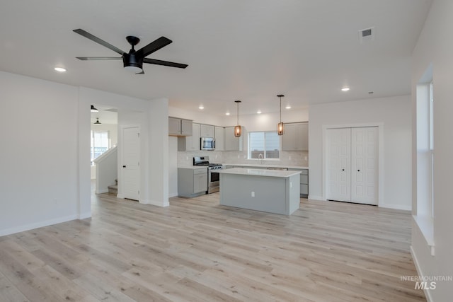 kitchen with light wood-type flooring, stainless steel appliances, a center island, ceiling fan, and gray cabinetry