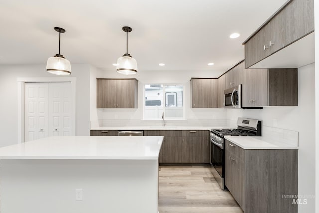 kitchen featuring light wood finished floors, light countertops, appliances with stainless steel finishes, and a sink