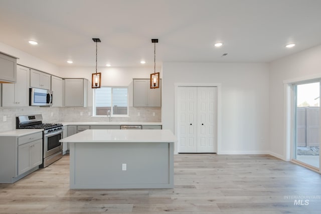 kitchen featuring gray cabinets, a kitchen island, decorative backsplash, appliances with stainless steel finishes, and light hardwood / wood-style floors