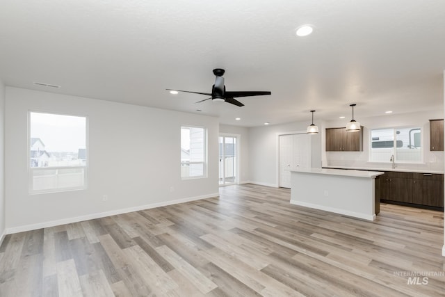 kitchen featuring light wood-style flooring, open floor plan, a center island, light countertops, and a sink